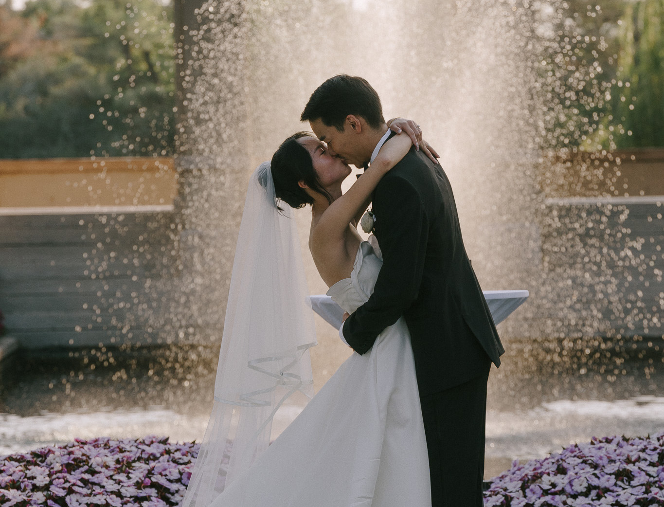 happy bride and groom kissing in front of fountain